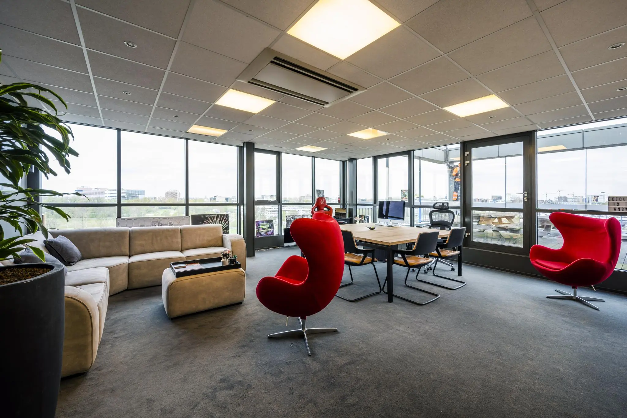 Moderne kantoorruimte aan de Anthony Fokkerweg met grote ramen, een vergadertafel, loungesofa en opvallende rode stoelen.